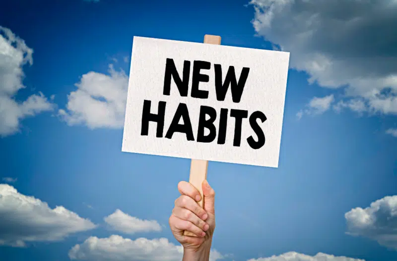 A hand holding a sign that reads new habits with a blue sky background.