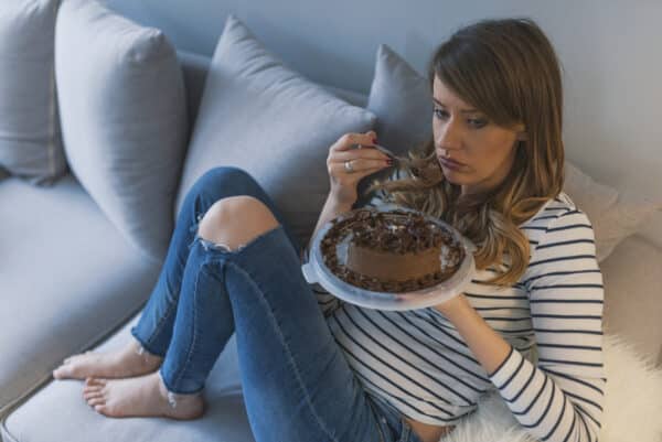 Woman curled up on a comfortable sofa eating a whole chocolate cake.