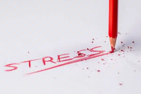 Red pencil wrote the word stress on a white piece of paper with red pencil flakes around.