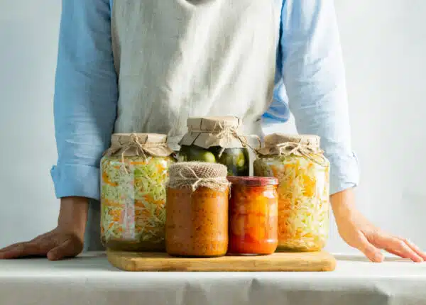 Person in an apron with various jars of fermented food in front of them.