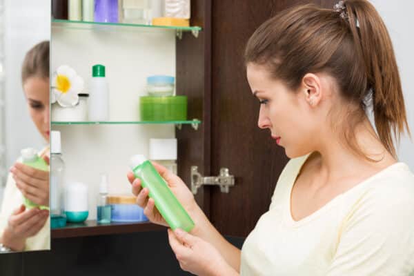 Woman standing in front of a medicine cabinet holding a beauty product bottle.
