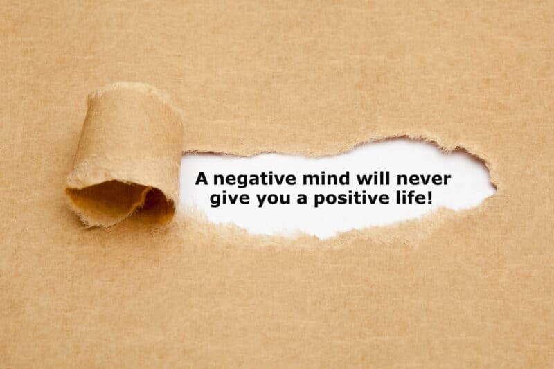 Tips to develop a positive mindset. Brown paper torn to reveal white paper underneath with the text "a negative mind will never give you a positive life!"