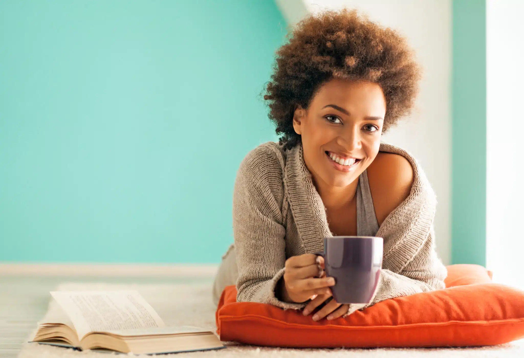 beautiful young woman lying down on a pillow drinking a cup of coffee